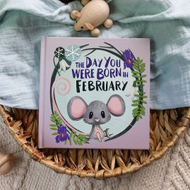 The book cover for Day You Were Born In February in a seagrass tray. A playful, illustrated mouse sat down surrounded by seasonal flowers.