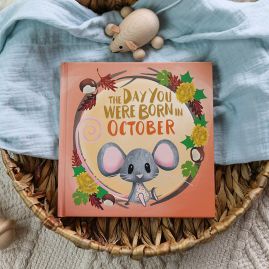 The book cover for Day You Were Born In October. A playful, illustrated mouse sat down surrounded by autumnal leaves and conkers.