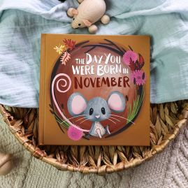 The book cover for Day You Were Born In December. A playful, illustrated mouse sat down surrounded by autumnal leaves and chrysanthemum flowers.
