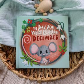 The book cover for Day You Were Born In December. A playful, illustrated mouse sat down surrounded by hollies and December flowers.